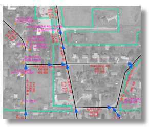 A grayscale map showing a neighborhood with property lines in green, street names, and utility information in red and blue text and arrows, designed using GIS for E911 emergency response planning.