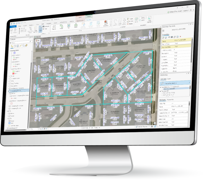 arcgis pro parcel fabric migration A computer monitor displays mapping software showing an aerial view of a neighborhood with labeled parcels and property boundaries, illustrating the arcgis pro parcel fabric migration process.