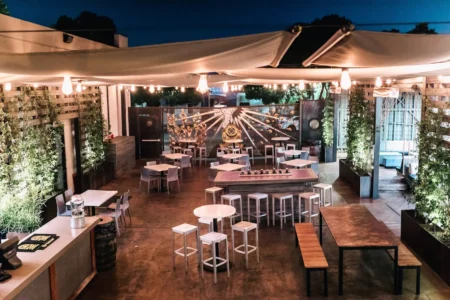 Open-air patio dining area at Sidwell at UC 25ac, featuring string lights, greenery on the walls, various tables and chairs, and a modern, casual atmosphere at dusk.