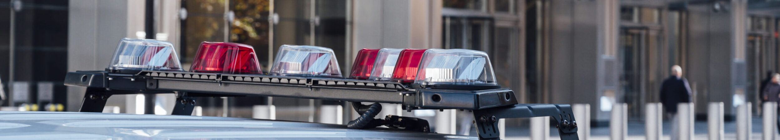 Close-up of the roof of a police vehicle with red and blue emergency lights, parked in front of a modern glass building—highlighting the crucial role of public safety GIS in urban law enforcement.